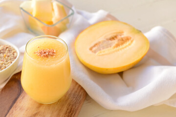Glass with melon smoothie on light wooden background