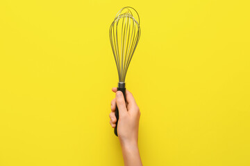 Female hand with whisk on color background