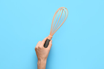 Female hand with whisk on color background