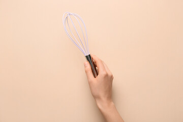 Female hand with whisk on color background