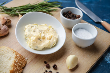 Bowl with garlic butter and ingredients on color background, closeup