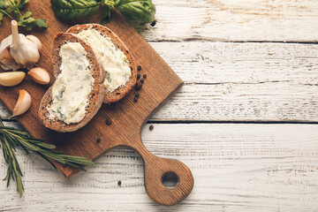 Board with slices of bread and garlic butter on light wooden background