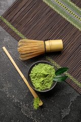 Bowl with powdered matcha tea, chasen and chashaku on dark background
