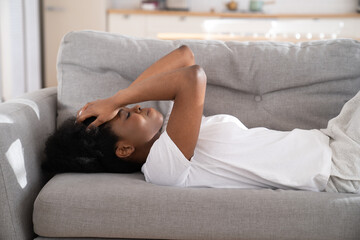 Obraz premium Sad depressed young African woman lying on couch at home crying, feeling loneliness, suffering from breakup. Upset Black girl has mental problems, can not forget her boyfriend. Relationship problem.