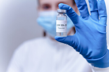 Obraz premium Female doctor wearing a protective mask holding a bottle of COVID-19 vaccine