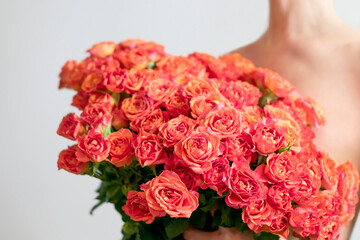 Fragment of a naked girl on a gray background, covering her body with a bouquet of roses. No recognizable people on photo