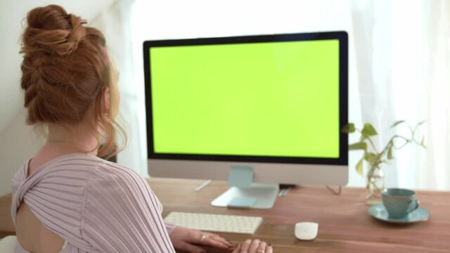 Green Screen Monitor. Beautiful Lady Sitting at her Desk using personal Computer. Over Shoulder Shot filmed in 4K. Chroma Key Mock-up for application, website, digital business and home office.