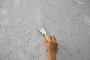 Hand with putty knife make by putty interesting diverse grey texture on wall. Abstract background...