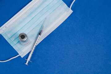 Vial of Covid-19 vaccine, syringe for injection, blue mask on a blue background.