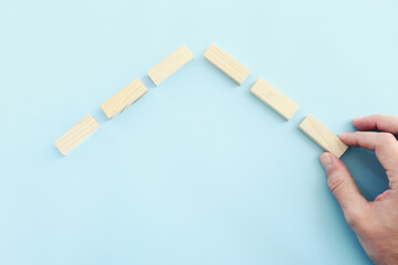 man's hand building ahouse made from wooden blocks over blue patel background