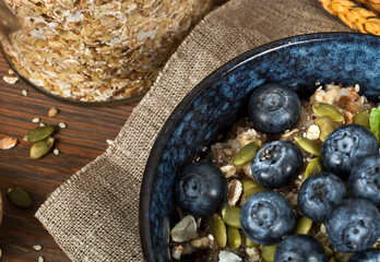Oatmeal porridge with blueberries and seeds in a blue ceramic bowl and a glass jar of oat flakes on a wooden background. Healthy eating concept. Top view.