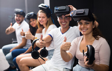 Group of friends are wearing virtual reality goggles and giving thumbs up.