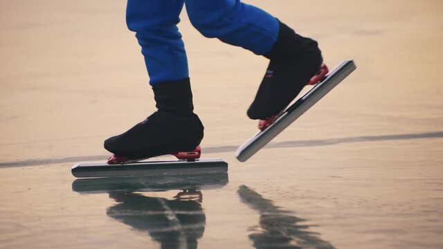 The child train on ice speed skating. The legs in skates close up. The kid girl skates in the winter in sportswear, sport glasses. Children speed skating short long track. Outdoor slow motion 180fps.