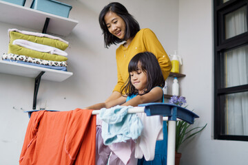 Beautiful young asian woman and child girl little helper drying clothes doing laundry at home.