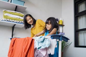 Naklejka na ściany i meble Beautiful young asian woman and child girl little helper drying clothes doing laundry at home.