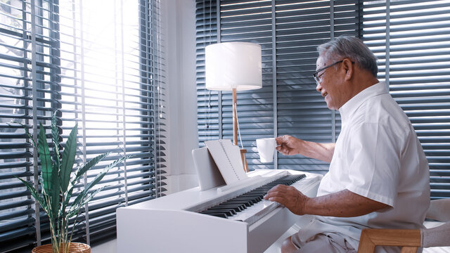 An Elderly Asian Man Practicing Playing The Piano In The Living Room Of His Home After Retirement From Work.