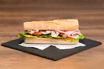 Select focus of a delicious looking meat and vegetables sub sandwich on a slate tray