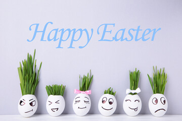 Cute handmade eggs with hair of green grass with copy space. Easter concept on grey background