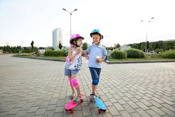 Little boy in a helmet hugs a girl in the Park, they ride a skateboard and eat ice cream