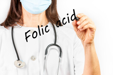 Doctor with mask writing the word folic acid on a white background