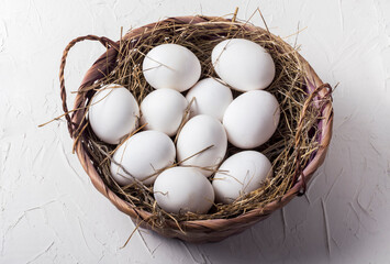 ten chicken white eggs in a basket with hay on a white background