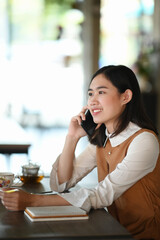 Portrait os young female sitting in coffee shop and talking o mobile phone.