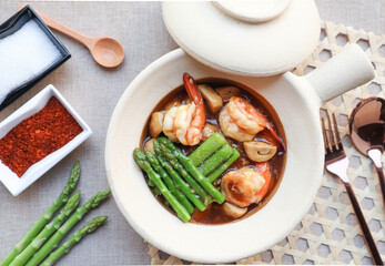 Stir-fried rice noodles with shrimp, asparagus and mushroom in gravy sauce serving in clay pot ( Thai food called Rad na Koong) - Top view on the bamboo placemat