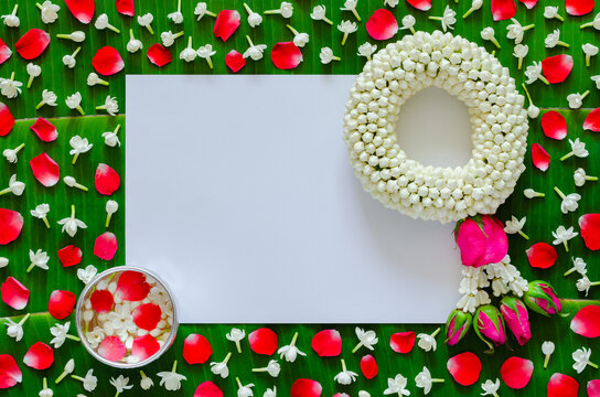 White blank paper with jasmine garland and flowers in water bowl on banana leaf background for Songkran festival.