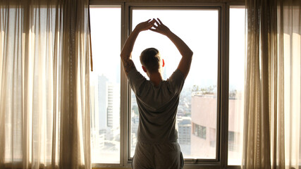 Handsome young man stretching on a Sunny Morning in a Hotel Room, a Man Looking on the Window...