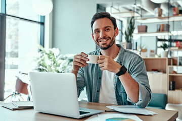 Smiling businessman drinking coffee in cafe and looking at camera