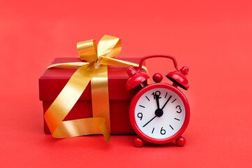 Red alarm clock and red gift box on red background