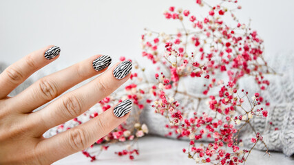 Hand in sweater and pink flowers with zebra animal printed nails. Female manicure. Glamorous...