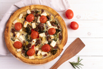 Quiche with broccoli, meat, tomato and brined cheese. On a white wooden table. Top view.