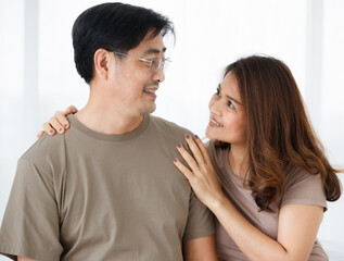 Horizontal portrait shot of senior Asian lover couple wearing eyeglasses embracing together. Wife stands behind her husband to hug and snuggle him with love. Concept of love on Saint Valentine's Day.