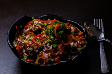 High angle shot of delicious Chilli chicken in black bowl on wooden surface.
