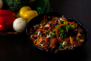 Tasty Chilli chicken with colorful vegetables on wooden surface.