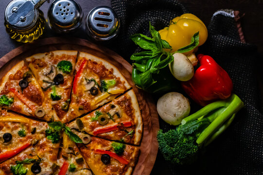 Top view close up of delicious pizza along with vegetables kept on dark cloth.