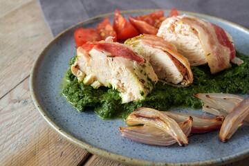 Chicken breast wrapped in bacon on cream spinach with baked onions and tomatoes on a blue plate and a rustic wooden table
