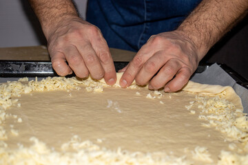 The hands of the cook who put grated cheese on the dough he rolls.