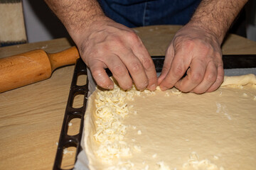 The hands of the cook who put grated cheese on the dough he rolls.