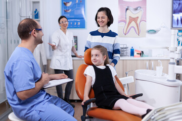 Dentist assistant giving good news to kid parent after teeth examination in dental office. Child with her mother during teeth check up with stomatolog sitting on chair.