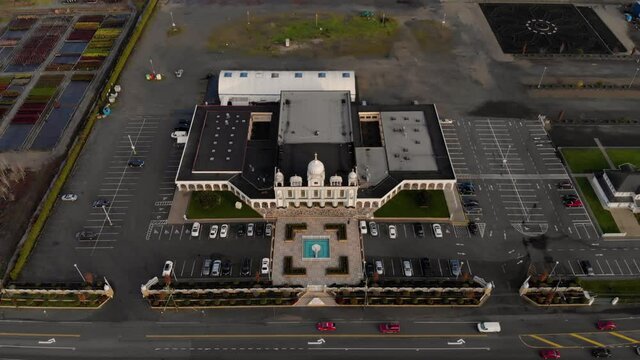 Drone 4K of front facade of Sikh temple with beautiful and elaborate sculpture and symmetrical architecture revealing the blueberry farmland and parking lots around the building