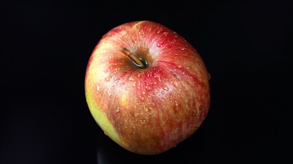 Close up of water droplets on shiny surface of fresh red apple on black background