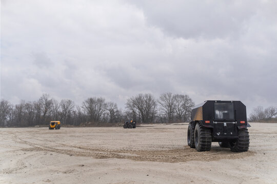 Three all-terrain vehicles with huge wheels driving in a sandy area