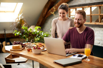 Happy couple using laptop after breakfast in dining room.