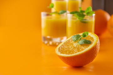 Half an orange and juice in glasses on an orange background. Close-up. Place for text. High quality photo.