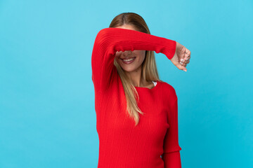 Young blonde woman isolated on blue background covering eyes by hands