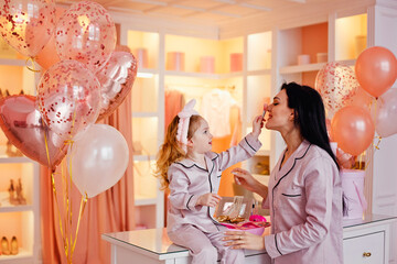 A young mother and her daughter in pajamas are laughing and having fun together in the bedroom and...