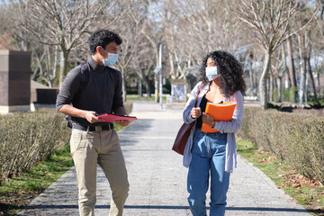 Two latin students walking in social distance wearing face mask looking at each other. New normal in the university campus.