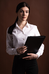 Serious brunette business woman with folder in hands on brown background in studio